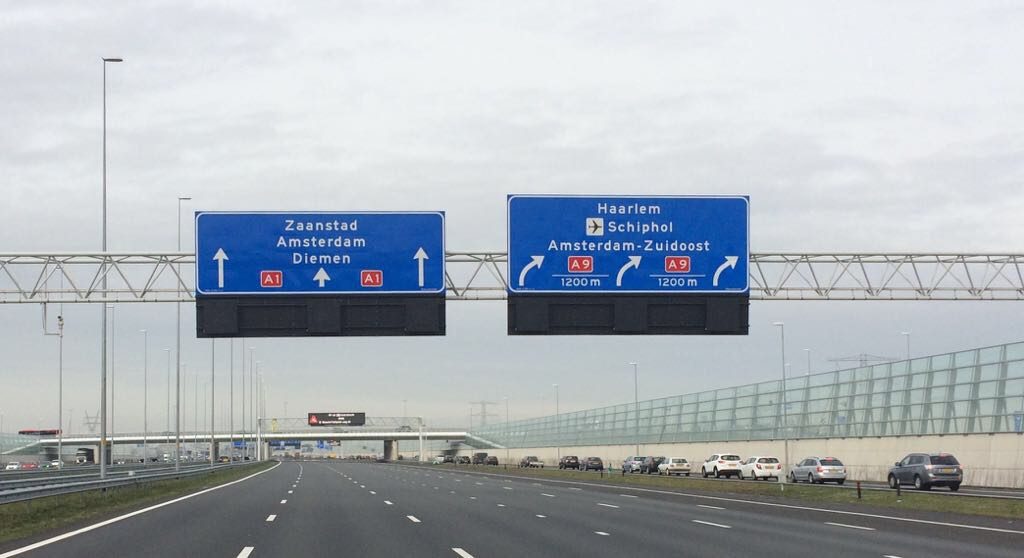 Snelweg met boven de weg blauwe verkeersborden waarom de richting staat aangegeven: rechtdoor is op de A1 blijven, rechtsaf is naar de A9 Haarlem/Schiphol/Amsterdam-Zuidoost