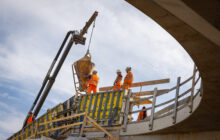 beton werkzaamheden, foto van onder naar boven genomen. Boven op de verdiepte ligging staan vier personen.