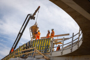 beton werkzaamheden, foto van onder naar boven genomen. Boven op de verdiepte ligging staan vier personen.