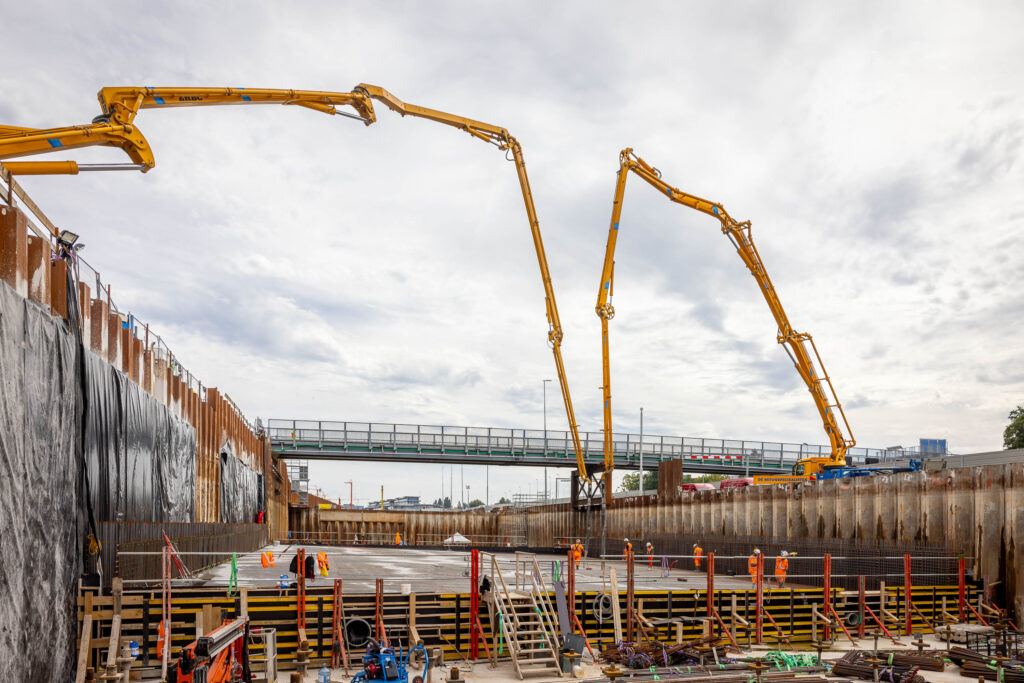 Foto genomen vanaf de bouwplaats met links en rechts grote gele kranen. 