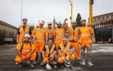 Een groepsfoto van 9 mannen op de bouwplaats die allemaal blij kijken.