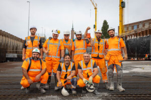 Een groepsfoto van 9 mannen op de bouwplaats die allemaal blij kijken.