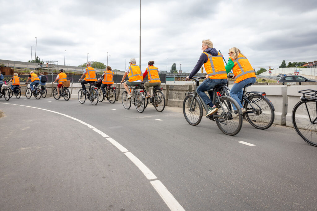 Een groep fietsende mensen met oranje hesjes aan.