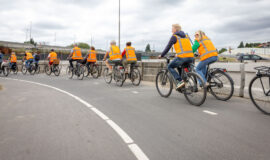 Een groep fietsende mensen met oranje hesjes aan.