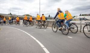 Een groep fietsende mensen met oranje hesjes aan.