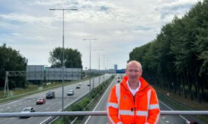 Verkeersmanager Bert Jan Zandhuis in een oranje jas op een viaduct over de A9, met de op de achtergrond de A9
