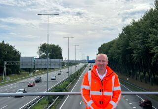 Verkeersmanager Bert Jan Zandhuis in een oranje jas op een viaduct over de A9, met de op de achtergrond de A9
