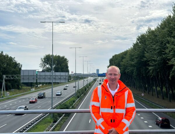 Verkeersmanager Bert Jan Zandhuis in een oranje jas op een viaduct over de A9, met de op de achtergrond de A9